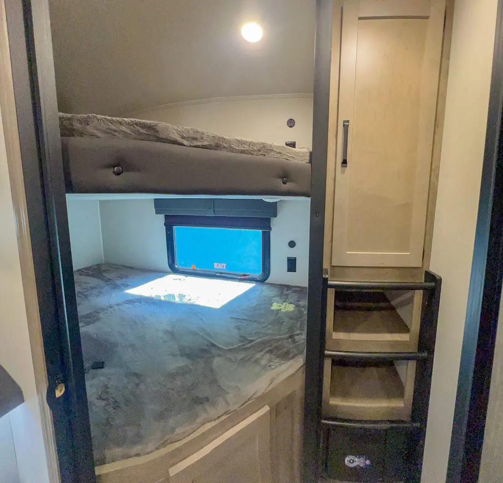 A compact room with a bunk bed, window, cabinet, and stairs.