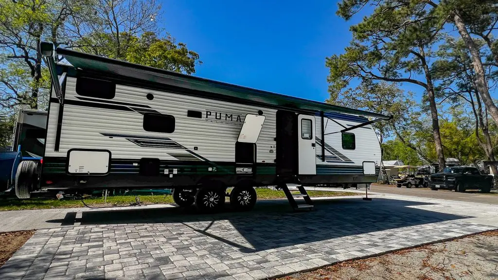 A large RV parked on a paved lot with trees and a blue sky in the background.