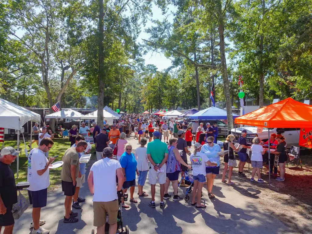 A large crowd of people gathered at an outdoor event with tents and trees in the background.