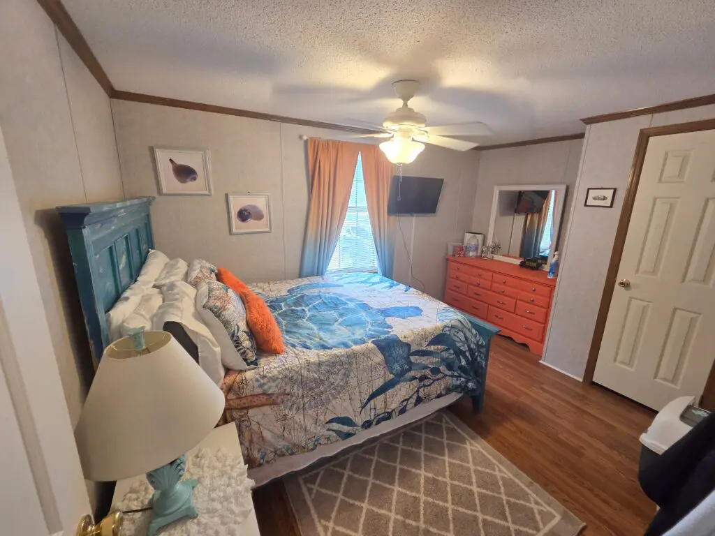 A wide-angle view of a guest room with a bed, dresser, lamp, and TV.