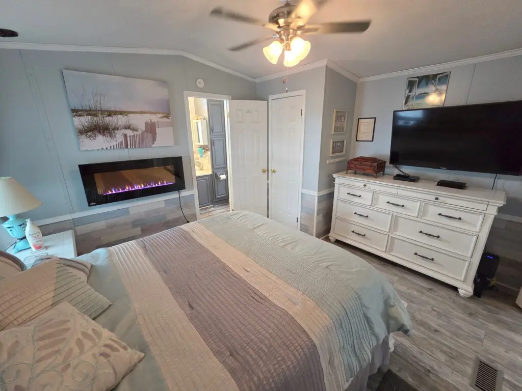 A wide-angle view of a guest room with a bed, TV, fireplace, and dresser.