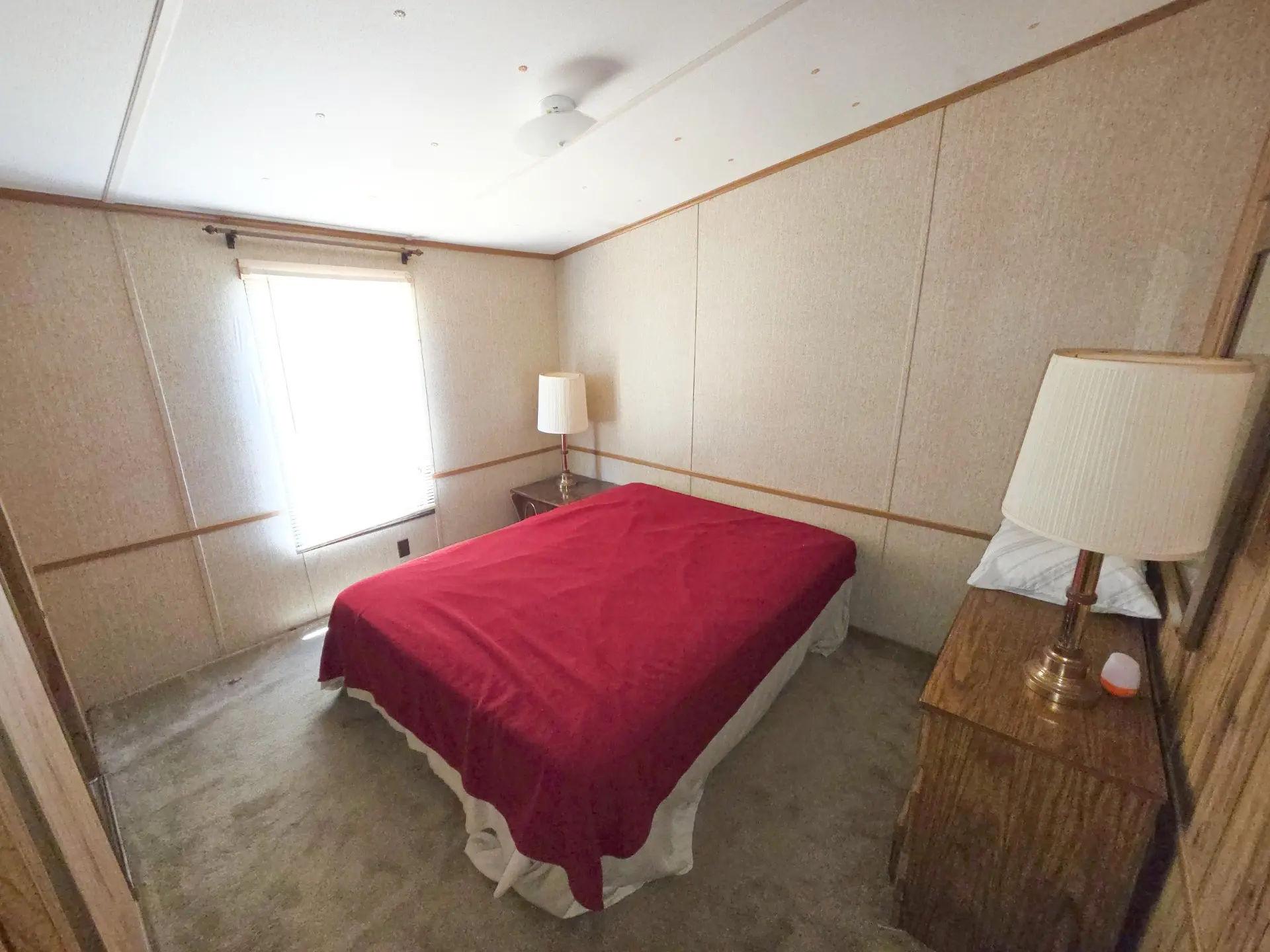 A small bedroom with a red bedspread, two nightstands with lamps, and a window.