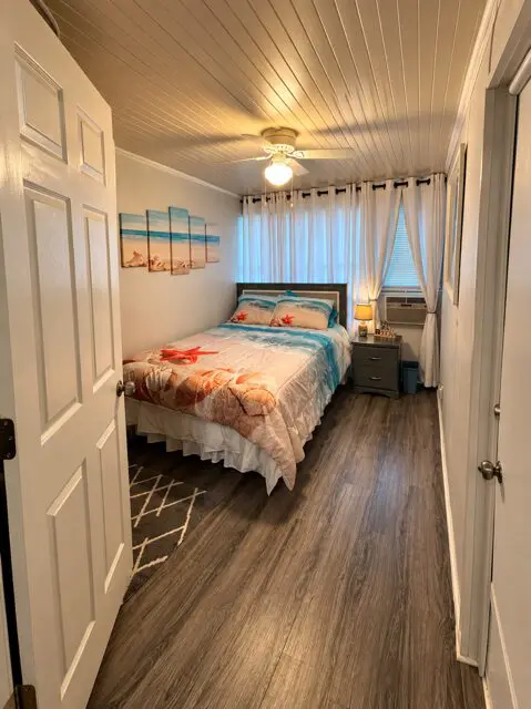 A small guest room with a bed, nightstand, and ceiling fan.