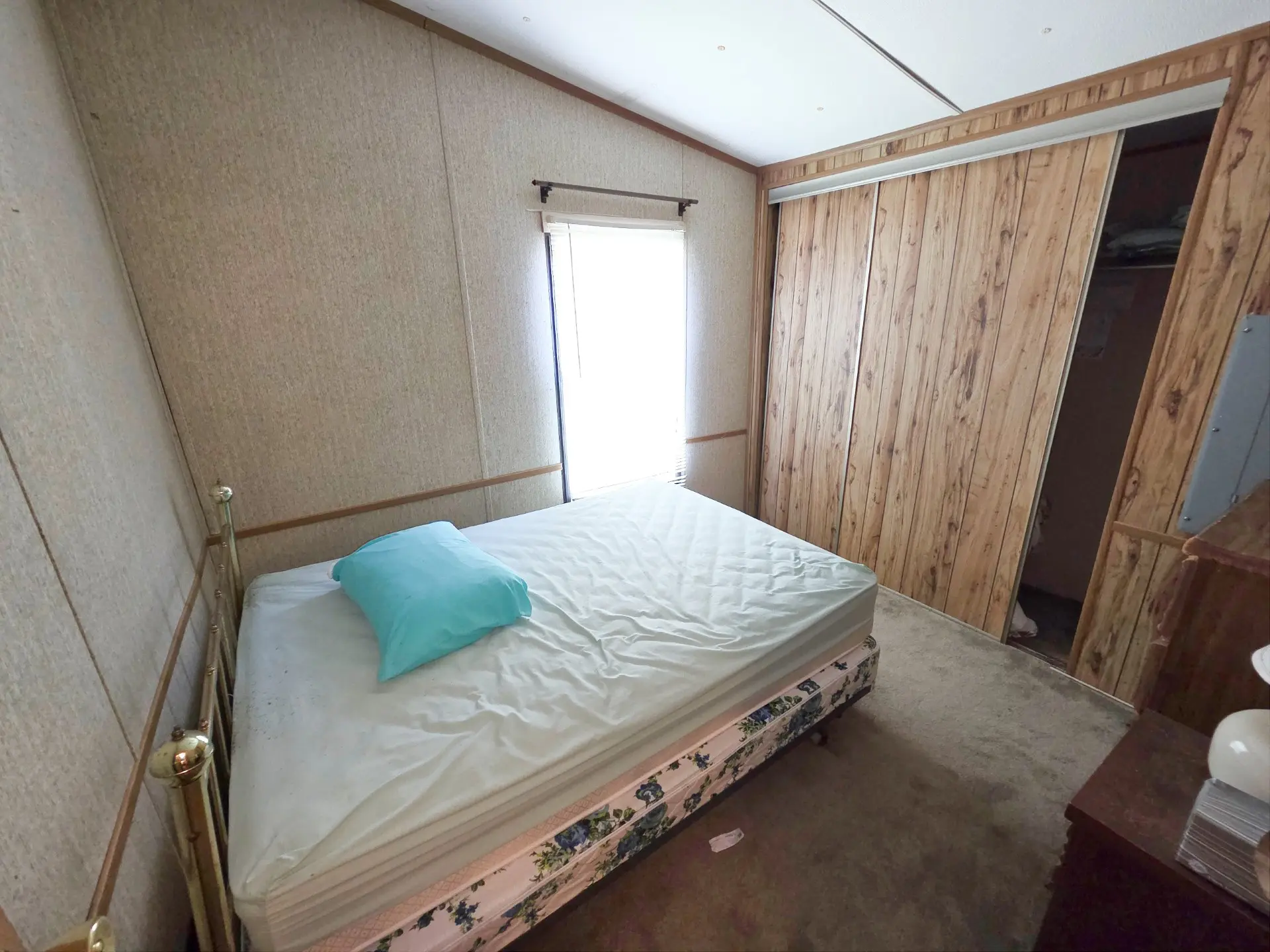 A small room with a bed, window, and wood paneling