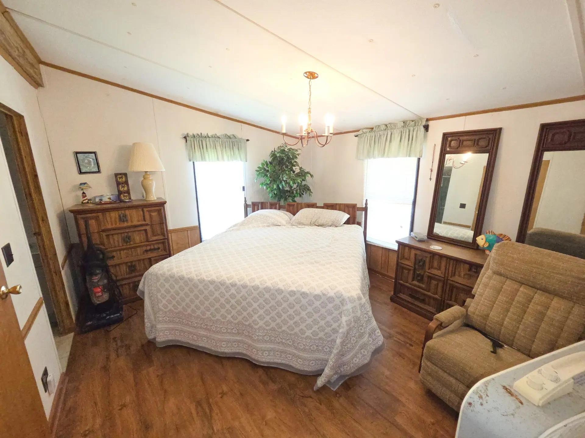 A wide-angle view of a hotel room with a bed, dresser, chair, and mirror.
