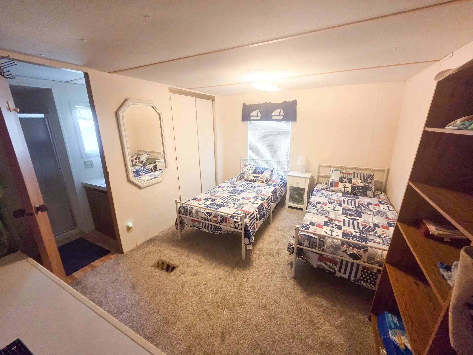 A room with two twin beds, a window, and a mirror on the wall.