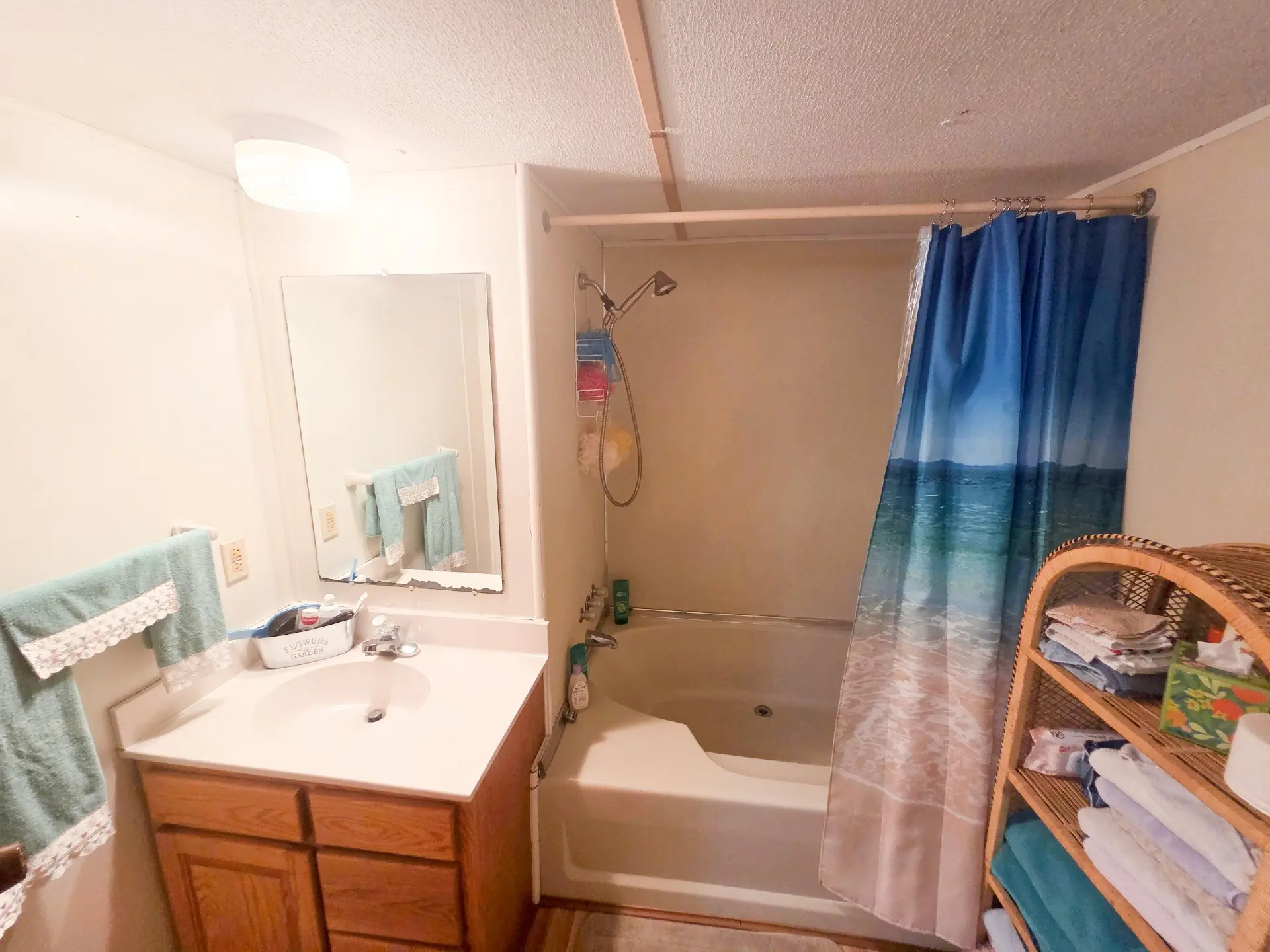 A bathroom with a sink, mirror, bathtub with shower curtain, and wooden cabinet.
