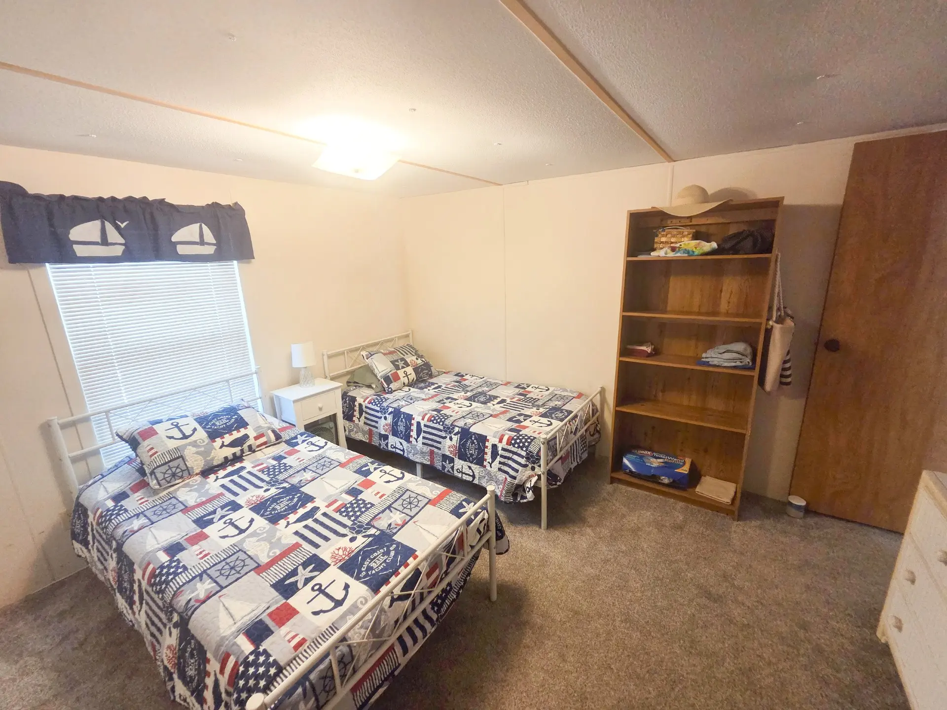 A room with two beds, a window, and a shelving unit.