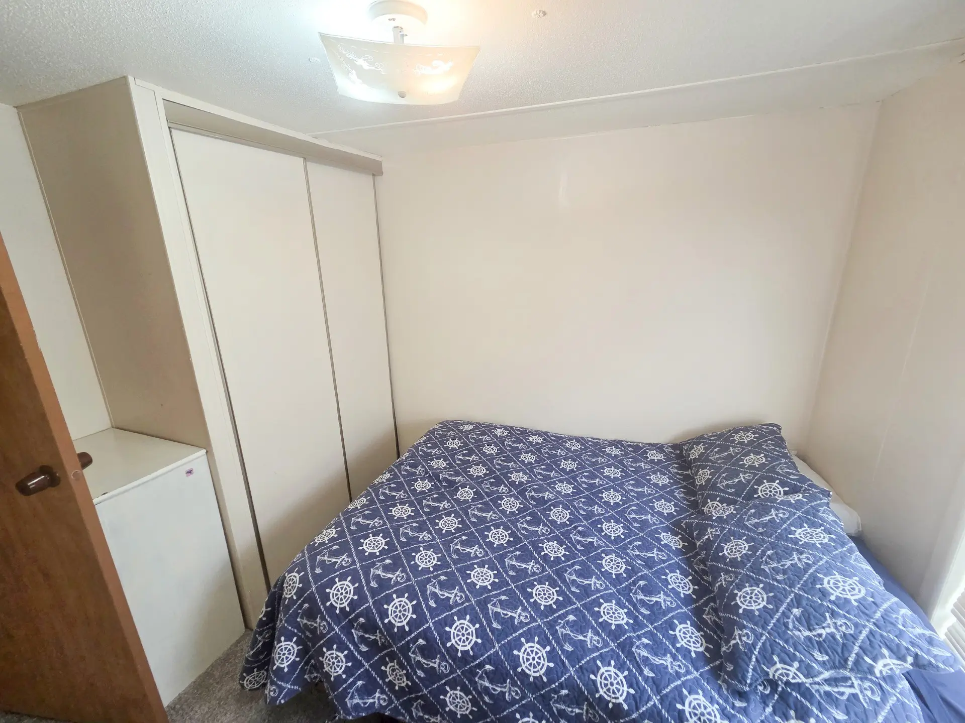 A small hotel room with a bed, closet, and mini-fridge.