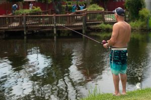 Man wearing swimsuit fishes alone at Crater Lake on a sunny afternoon in Lakewood Camping Resort
