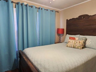 A neatly made bed with a dark wooden headboard and a red lamp beside it, in a room with beige walls and blue curtains.