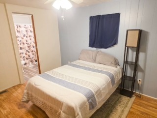 A wide view of a bedroom with a bed, lamp, and doorway.