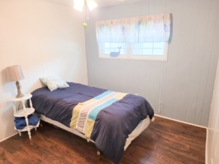 A small bedroom with a single bed, a nightstand with a lamp, and a window with a curtain.