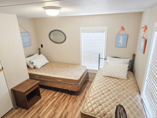 A room with two twin beds, a wooden floor, panel walls, and window blinds.