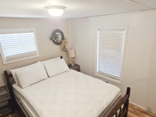 A small, simply furnished bedroom with a bed, two windows, and a nightstand.